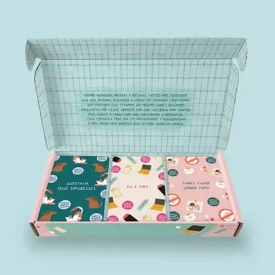 Caixa aberta com três livros coloridos com desenhos e texto em português