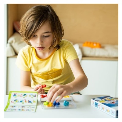 Criança a jogar jogo de tabuleiro com peças coloridas numa mesa branca