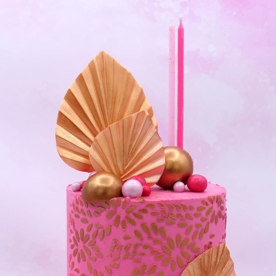 Bolo rosa decorado com padrão dourado, folhas douradas e velas rosas