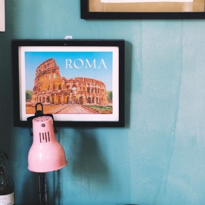 Quadro do Coliseu em Roma com texto ROMA numa parede azul e lâmpada rosa