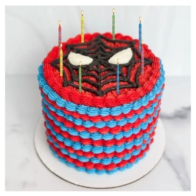 Bolo decorado em vermelho e azul com desenho de teia de aranha no topo e velas coloridas.