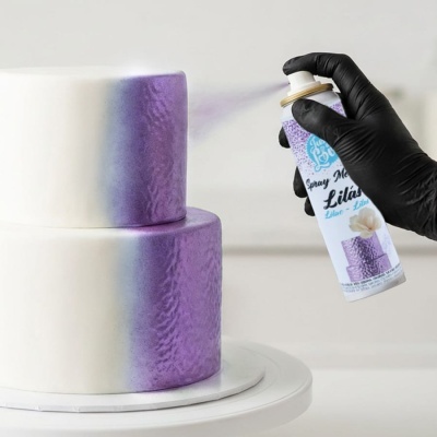 Bolo branco de dois andares com spray metálico lilás a ser aplicado