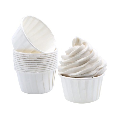 Pequenas formas de papel branco para bolos com um bolo decorado em branco.