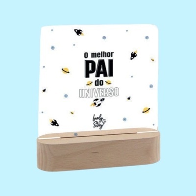 Luminária decorativa com base em madeira clara e painel de acrílico branco com desenhos de planetas e texto