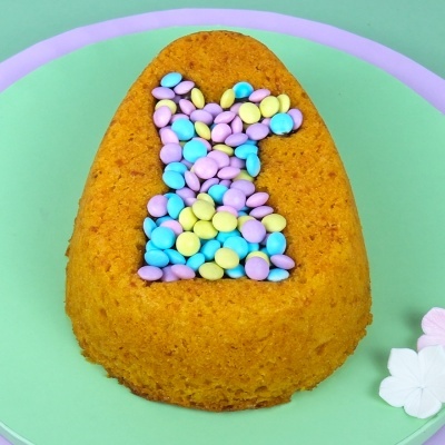 Bolo amarelo em forma de ovo com confeitos coloridos em forma de coelho num prato verde com borda roxa