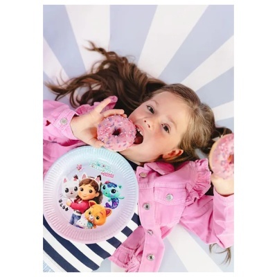 Criança com camisa às riscas e jaqueta rosa deitada segurando donuts cor de rosa e prato com personagens animadas.