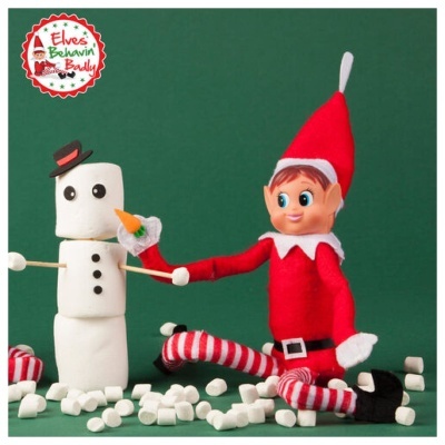 Elfo sentado ao lado de boneco de neve feito de marshmallows com fundo verde