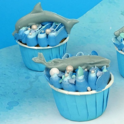 Cupcakes decorados com creme azul e figuras de tubarão cinza em forminhas azuis