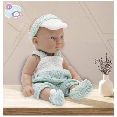 Boneca bebé com roupa de malha azul claro e branca sentada numa mesa de madeira junto a um vaso