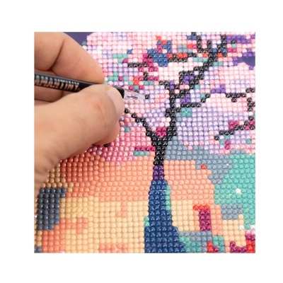 Mão aplicando cristais coloridos em padrão de árvore para arte diamantada