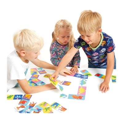 Crianças a jogar dominó de dinossauros coloridos numa mesa branca