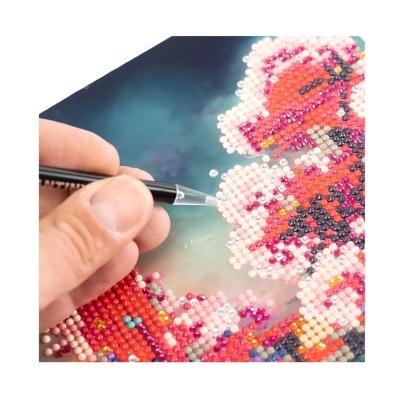 Pessoa aplicando pérolas coloridas numa tela para criar padrão floral