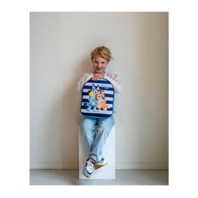 Criança loira com mochila azul e branca sentada num cubo branco