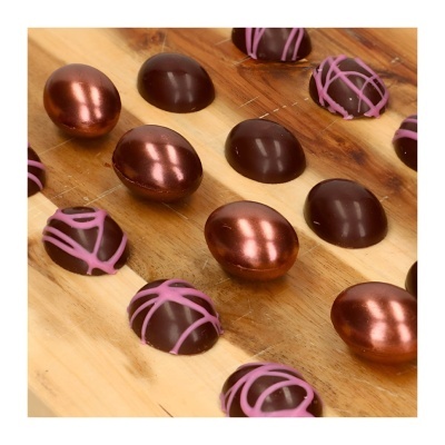 Ovos de chocolate metálicos bronze e bombons de chocolate preto com decoração lilás numa superfície de madeira.