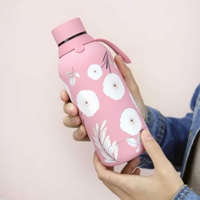 Garrafa térmica rosa com flores brancas e alça segurada por mãos