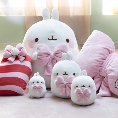 Peluches e almofadas brancas e rosa com laços e orelhas sobre chão interior