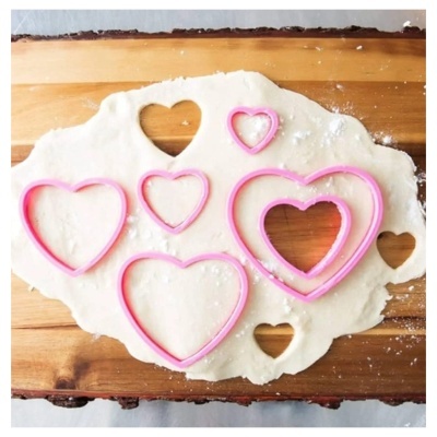 Conjunto de cortadores de bolachas em forma de coração rosa sobre massa branca numa tábua de madeira
