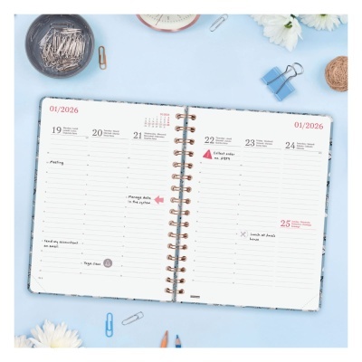 Agenda semanal aberta com espiral dourada sobre superfície azul clara com clips, lápis e flores brancas