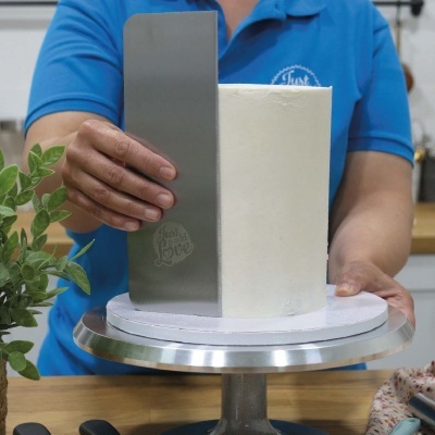 Espátula metálica alisando bolo branco numa cozinha