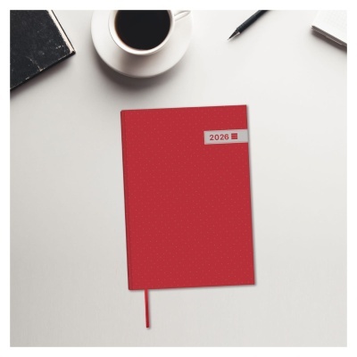Agenda vermelha com 2026 sobre mesa branca ao lado de caneca, caderno e caneta