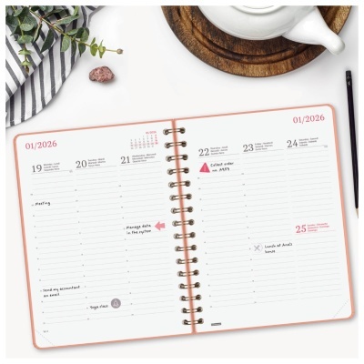 Agenda aberta com folhas brancas e texto, bule branco, base de madeira, lápis preto e tecido listrado