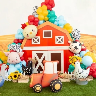 Decoração festa infantil com trator de tecido, balões coloridos, almofadas animais e celeiro vermelho.