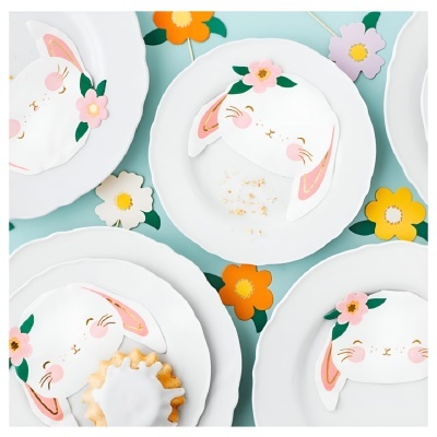 Pratos brancos com bolos decorados em forma de coelho e flores coloridas em fundo azul