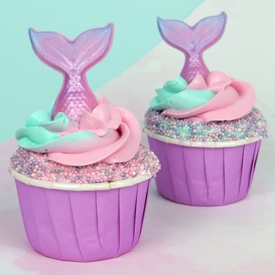 Dois cupcakes decorados com cauda de sereia roxa e cobertura colorida