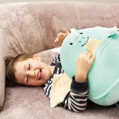 Criança deitada num sofá a abraçar uma almofada de peluche azul claro