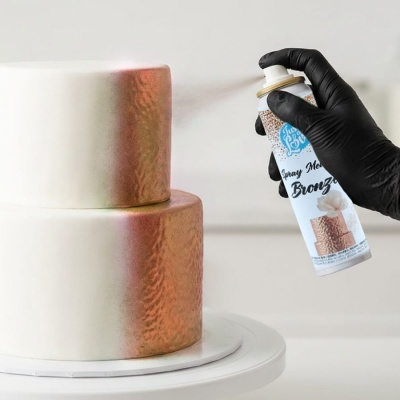 Bolo de dois andares a ser pulverizado com spray metálico bronze por mão com luva preta