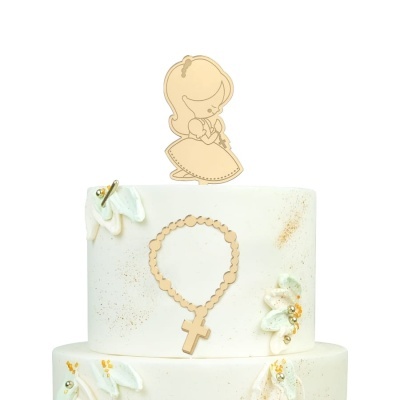 Bolo branco de dois andares com flores brancas e douradas, topo em forma de menina e terço dourado.