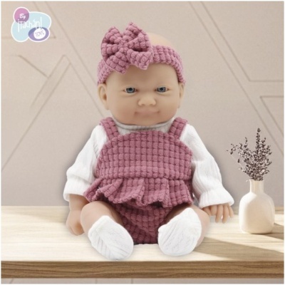 Boneca de bebé vestida com roupa de malha rosa e camisola branca sentada numa mesa de madeira