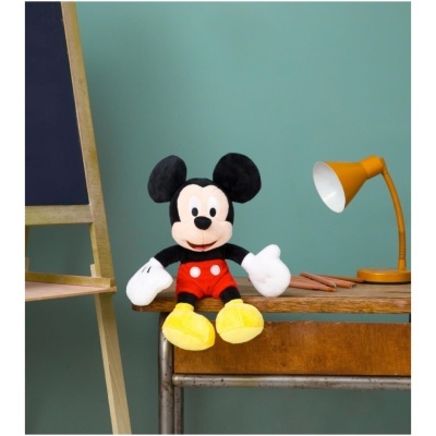 Boneco de peluche do Mickey Mouse sentado numa secretária com candeeiro amarelo e quadro-negro ao lado.