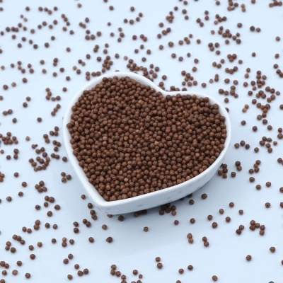 Taça branca em forma de coração cheia de pequenas pérolas marrons sobre fundo branco.