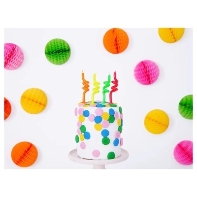 Bolo branco decorado com pontos coloridos e velas espiraladas em fundo branco com bolas decorativas coloridas.