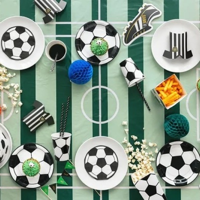 Artigos de festa de futebol com pratos, copos, tigela, toalha de mesa e balões coloridos