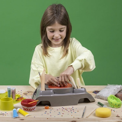 Criança a usar máquina de batik numa mesa com materiais de artesanato
