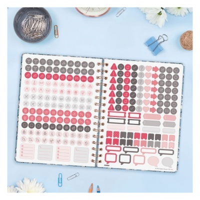 Livro aberto com autocolantes organizadores coloridos sobre mesa azul e objetos de papelaria