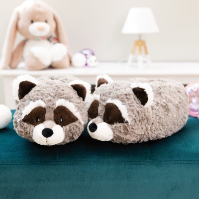 Chinelos de pelúcia em forma de guaxinim cinzentos com detalhes castanhos e brancos sobre superfície verde