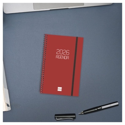 Agenda 2026 vermelha com espiral e elástico preto sobre mesa azul com caneta preta