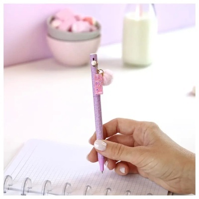 Caneta rosa com penduricalho e mão segurando sobre caderno quadriculado