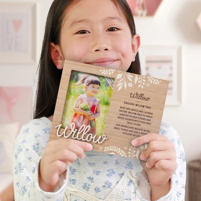 Menina segurando moldura de madeira com fotografia e texto em inglês sobre árvore Willow