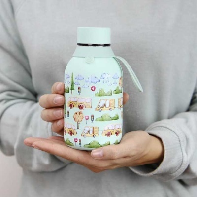 Garrafa térmica decorada com padrão de autocarros e árvores a ser segurada por duas mãos.
