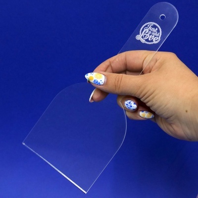 Espátula transparente de plástico com texto gravado, mão a segurá-la sobre fundo azul