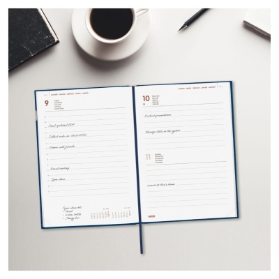 Caderno aberto com anotações, caneca de café, caneta e livro sobre uma mesa branca