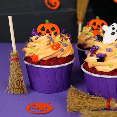 Cupcakes decorados com tema de Halloween e vassouras pequenas sobre superfície roxa