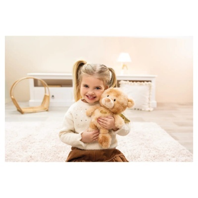 Menina loira a segurar ursinho de peluche castanho com asas douradas num quarto acolhedor