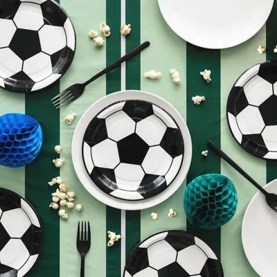 Mesa com pratos decorativos de bola de futebol e garfos pretos, com decoração colorida e pipocas