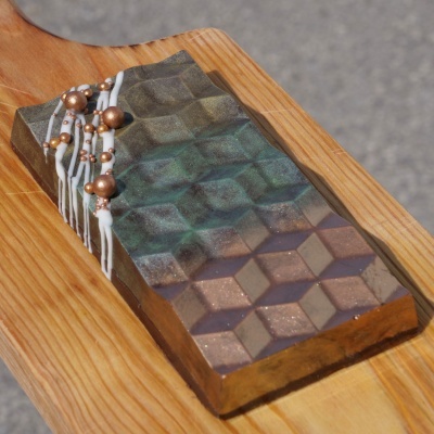 Barra de chocolate decorada com padrão geométrico e gotas decorativas sobre tábua de madeira