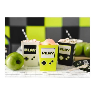 Três copos coloridos com texto PLAY e símbolo de comando, com snacks e maçãs verdes ao redor.